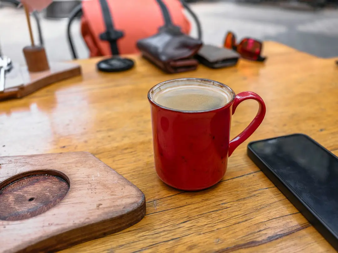 Red coffee mug on a wooden table beside a smartphone lying with its screen dark