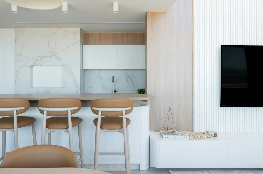 Bright open-plan apartment with a wall-mounted TV switched off beside a kitchen counter and bar stools